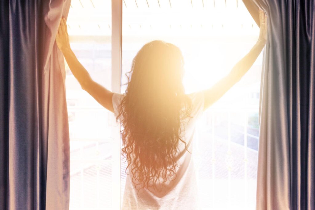 カーテンを開けて朝日を浴びる女性