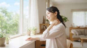 夏の朝、体のだるさを感じながら首や肩に手を添える女性。夏バテと思いがちな疲れが体からのサインであることをイメージした写真。