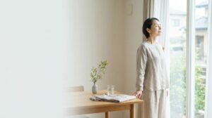 秋の朝にカーテンを開け、毎日の生活リズムを整える女性