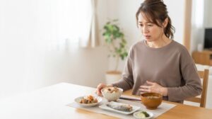 食欲の秋に胃の重さを感じ、食事の手を止める女性